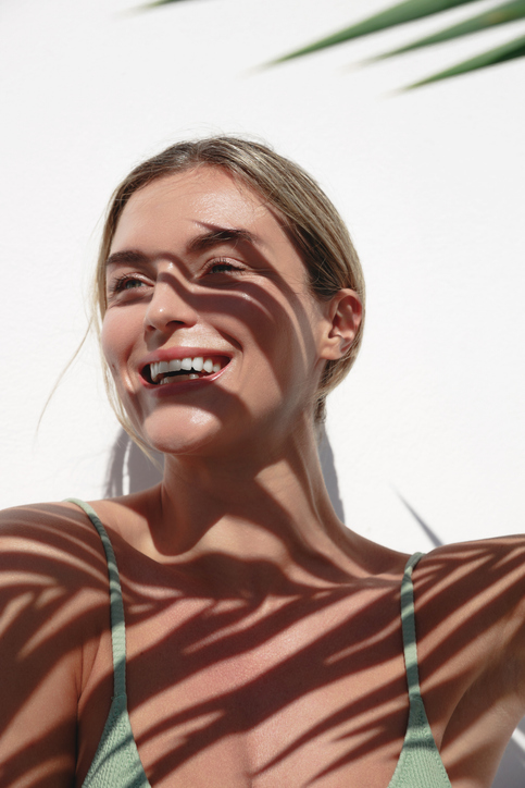 Kontakt young woman with shadow of palm leaves on white wall