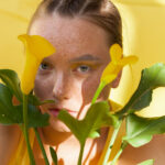 young beautiful woman with the face of freckles wearing in yellow dress near background with afternoon shadows.