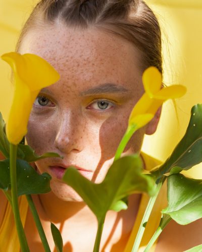 young beautiful woman with the face of freckles wearing in yellow dress near background with afternoon shadows.